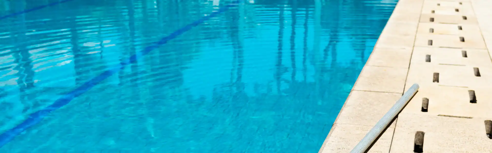 A close-up view of a swimming pool with clear blue water, showing pool lane lines and the edge with drainage grates, built by an experienced Excavation Contractor Suffolk County, NY.
