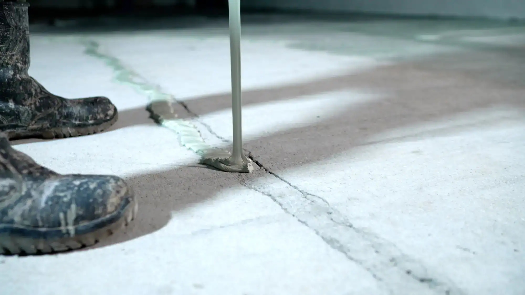 A close-up of a worker&rsquo;s boots on a concrete floor as a sealant is poured into a crack, repairing the surface&mdash;typical work for an Excavation Contractor Suffolk County, NY.