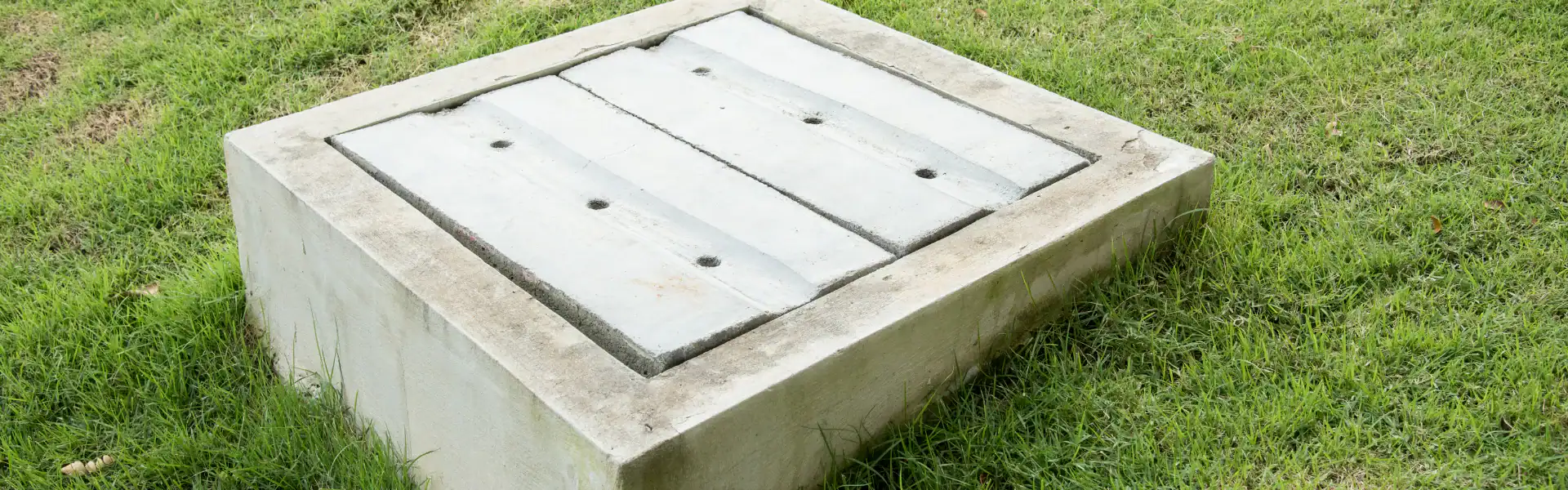 A concrete septic tank cover with three rectangular panels and several holes is set in a grassy lawn, expertly installed by an Excavation Contractor Suffolk County, NY.