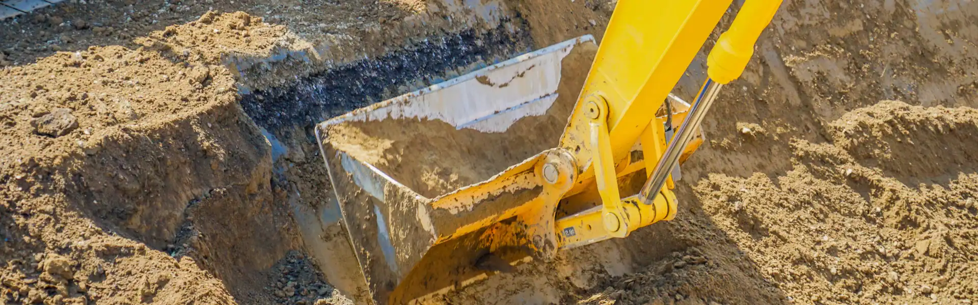 A yellow excavator bucket scoops up dirt at a NY construction site, with soil and sand surrounding the digging area—perfect work by an expert Excavation Contractor Suffolk County.