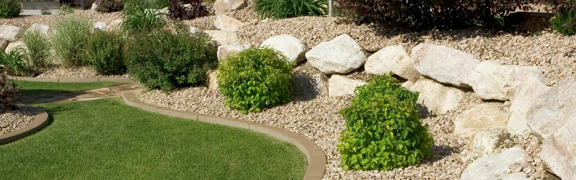 A landscaped garden with a neatly edged lawn, green shrubs, light-colored rocks, and decorative gravel—expertly crafted by an Excavation Contractor in Suffolk County, NY—creates a clean, organized appearance.
