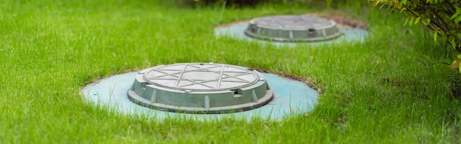 Two round septic tank covers are set in a grassy lawn, each surrounded by a patch of trimmed grass—an example of the clean, precise work done by an experienced Excavation Contractor Suffolk County, NY.