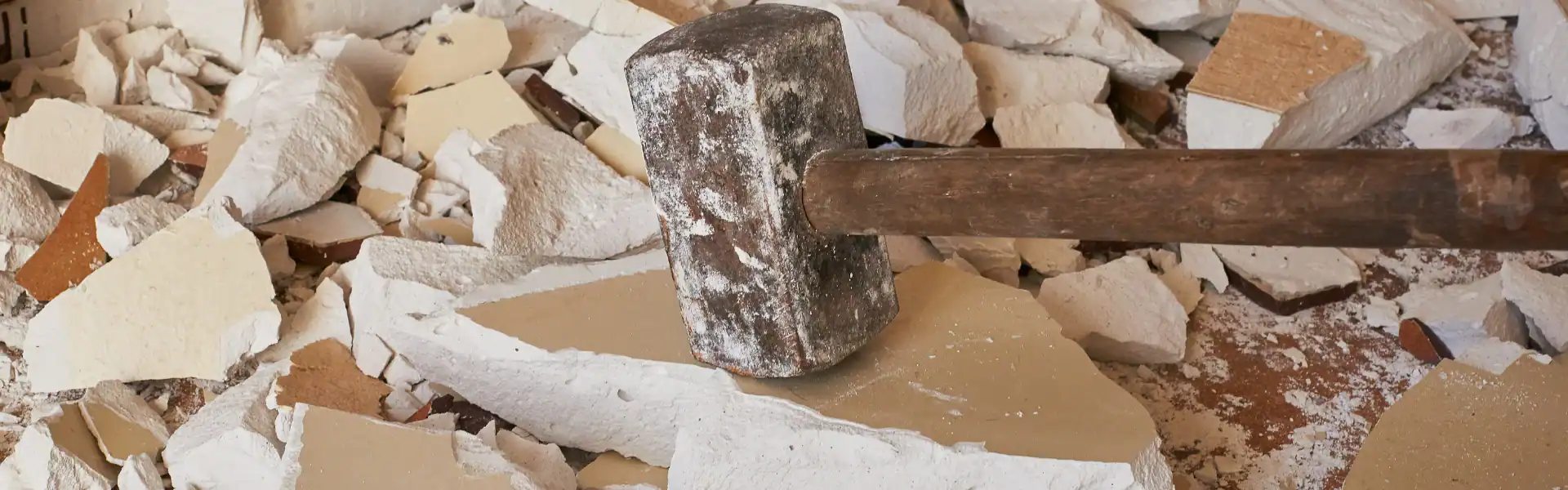A sledgehammer with a wooden handle rests on broken drywall and debris, suggesting ongoing demolition or construction work by an Excavation Contractor in Suffolk County, NY.