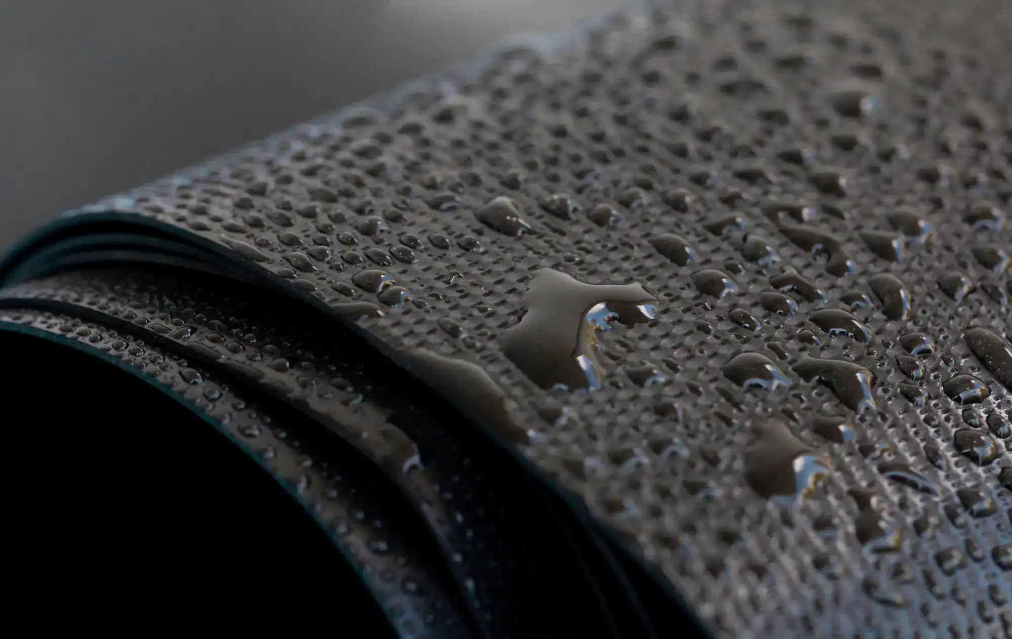 Close-up of water droplets on a textured, dark waterproof fabric, showcasing its water-resistant properties&mdash;ideal for NY outdoor gear or clothing used by an Excavation Contractor in Suffolk County.